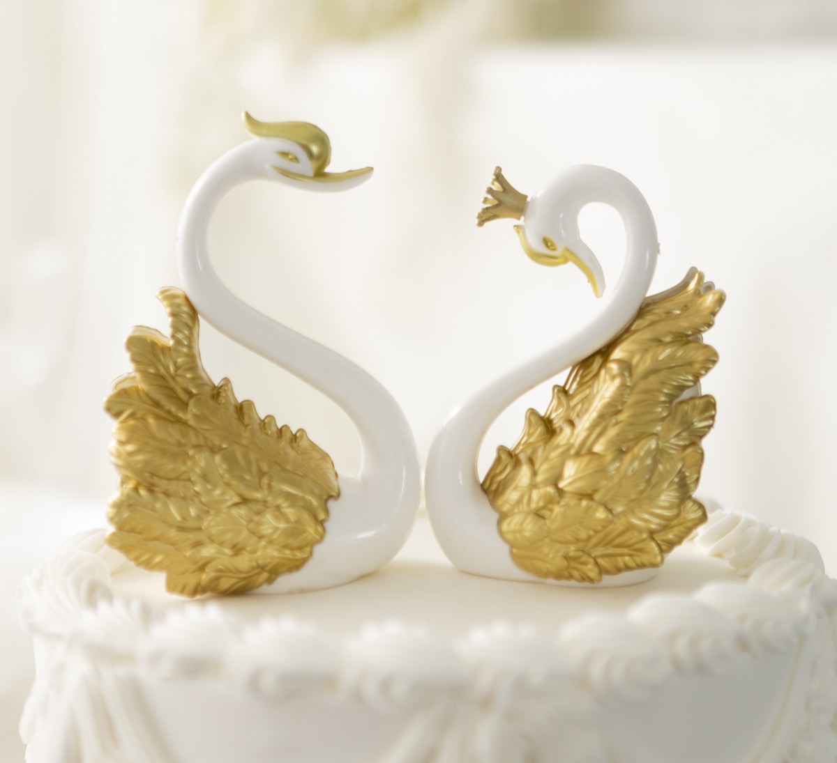 Two golden and porcelain swan figurines arranged together on top of a white icing wedding cake.